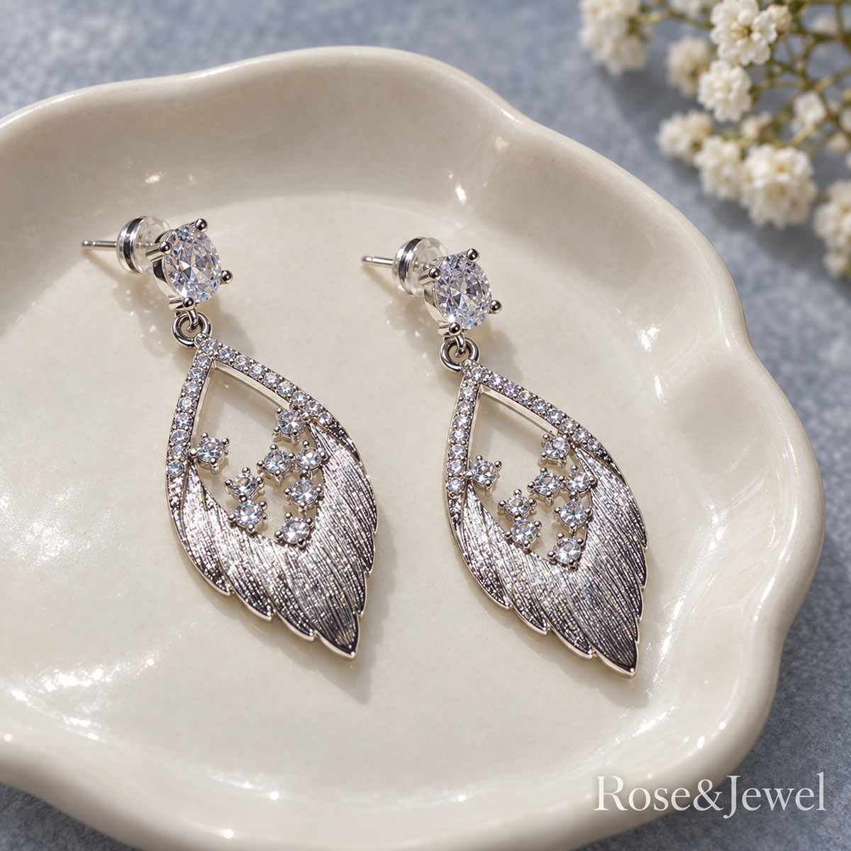 Matching feather drop earrings resting on a ceramic dish